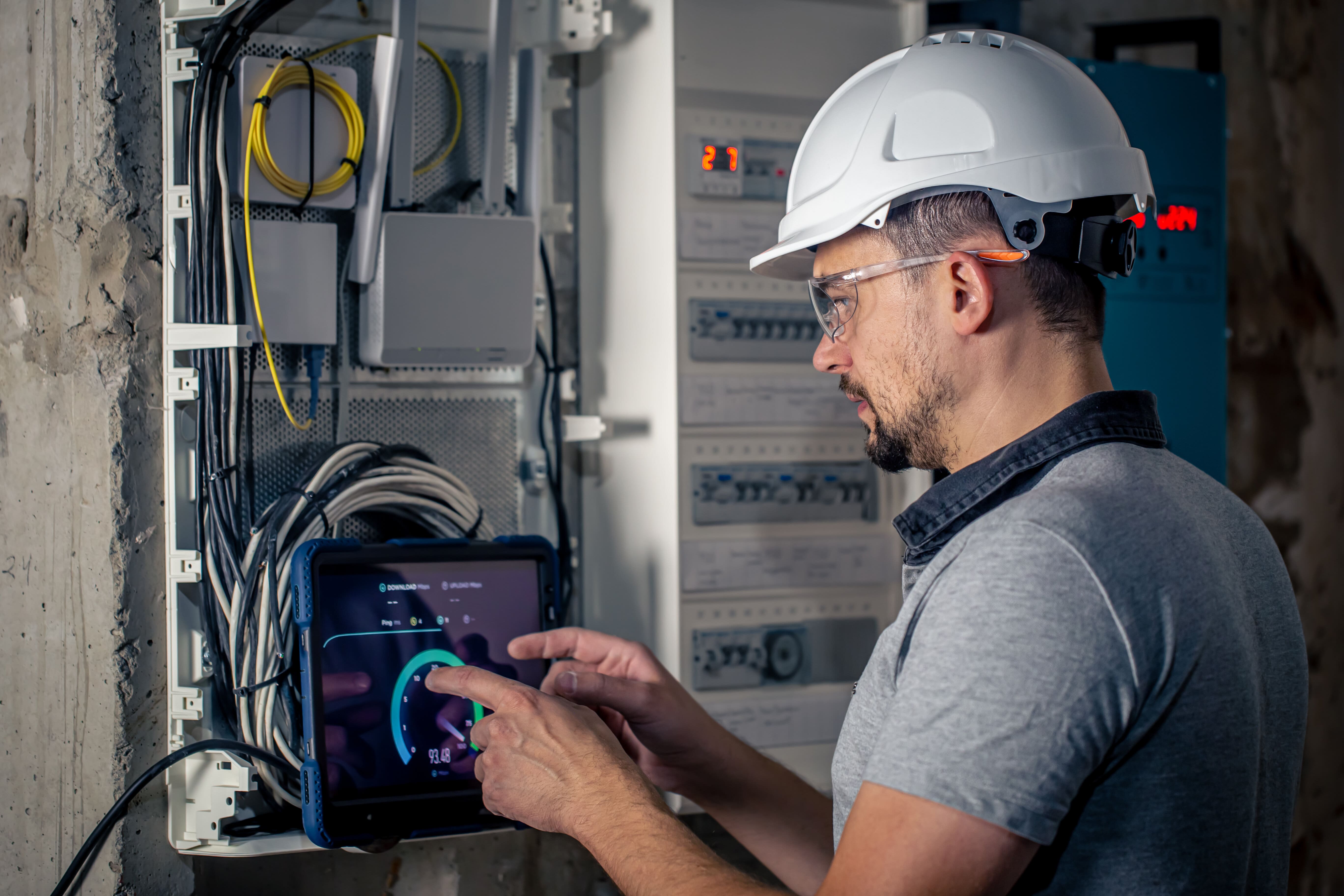 man electrical technician working switchboard with fuses uses tablet